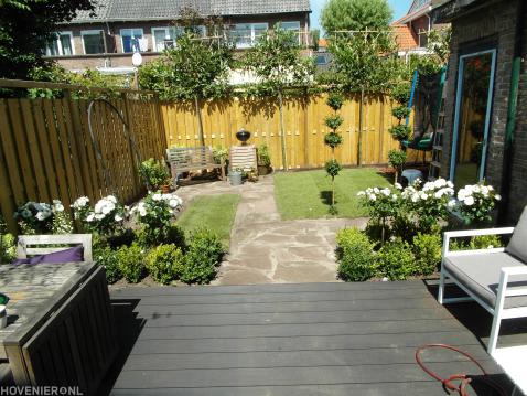 Achtertuin met vlonder, gazon, leibomen en tuinpad van flagstones