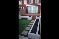 Achtertuin met houten vlonder, kunstgras en plantenbakken 2