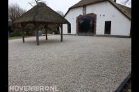 Overkapping met rieten dak en verharding van grind bij boerderij