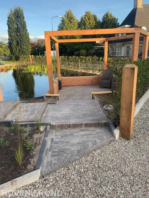 Zithoek met houten pergola bij vijver