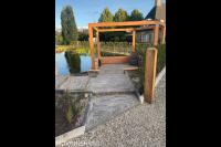 Zithoek met houten pergola bij vijver