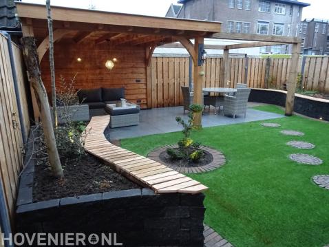 Tuin met houten terrasoverkapping, plantenbak en kunstgras