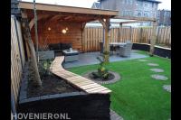 Tuin met houten terrasoverkapping, plantenbak en kunstgras