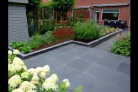 Achtertuin met bestrating van grote tegels en kleurrijke beplanting