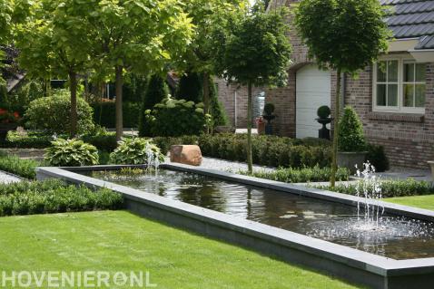 Strakke tuin met vijver en bomen.