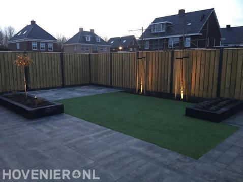 Achtertuin met bestrating, kunstgras, leibomen en houten schutting