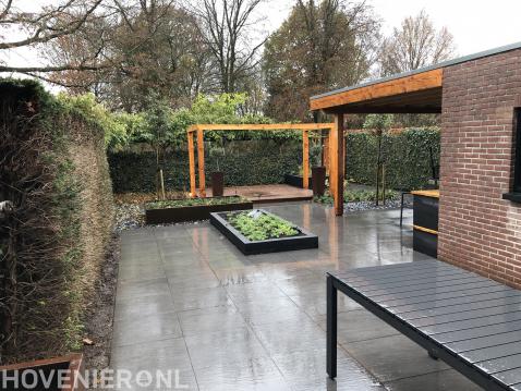 Tuinaanleg met sierbestrating, plantenbakken en houten pergola