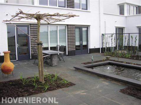 Strakke tuin met straatwerk van betontegels en vijver