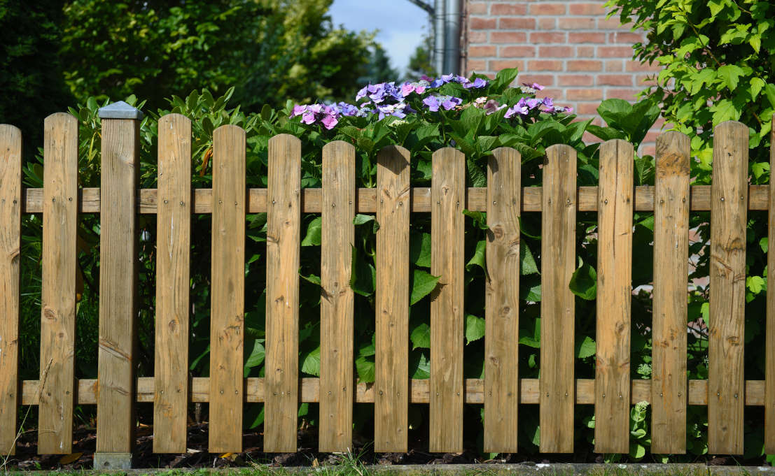 Laag houten tuinhek langs een border met hortensia's