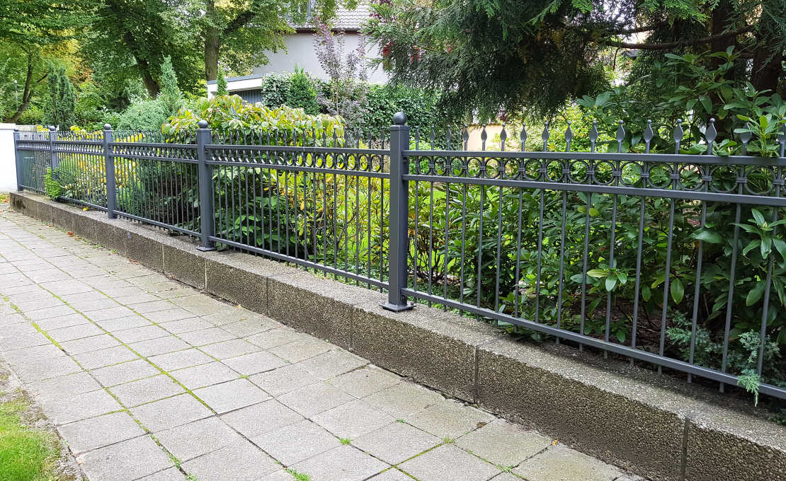 Antraciet metalen sierhekwerk met spijlen langs een stoep